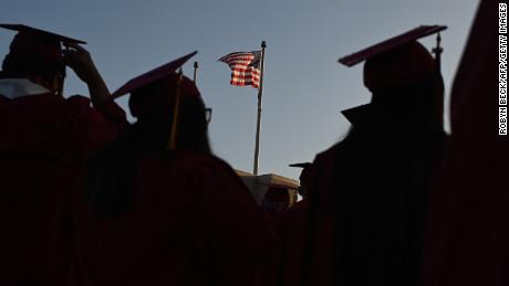 A US flag flies above a building as students earning degrees at Pasadena City College participate in the graduation ceremony, June 14, 2019, in Pasadena, California. - With 45 million borrowers owing $1.5 trillion, the student debt crisis in the United States has exploded in recent years and has become a key electoral issue in the run-up to the 2020 presidential elections.&quot;Somebody who graduates from a public university this year is expected to have over $35,000 in student loan debt on average,&quot; said Cody Hounanian, program director of Student Debt Crisis, a California NGO that assists students and is fighting for reforms. (Photo by Robyn Beck / AFP)        (Photo credit should read ROBYN BECK/AFP via Getty Images)